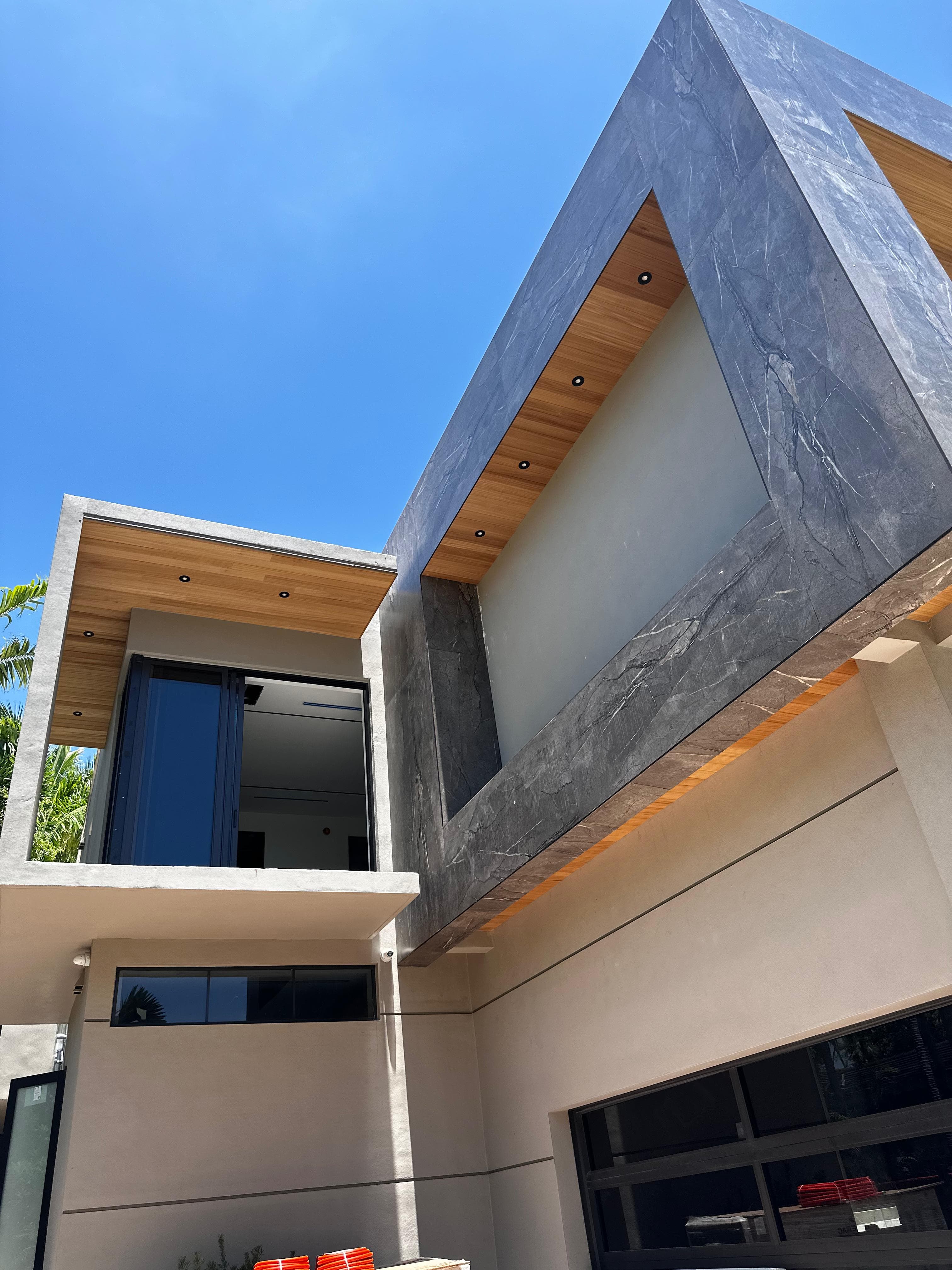 Architectural stone and wood roofline detail with recessed lighting on a high-end South Florida residence