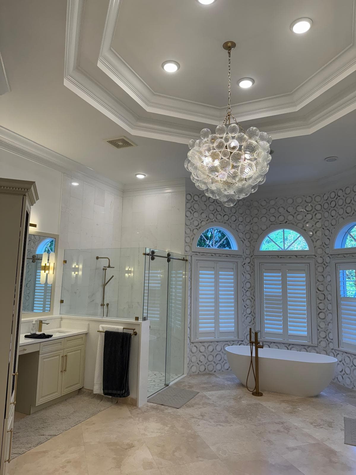 Residential primary bathroom with a decorative chandelier and tray ceiling