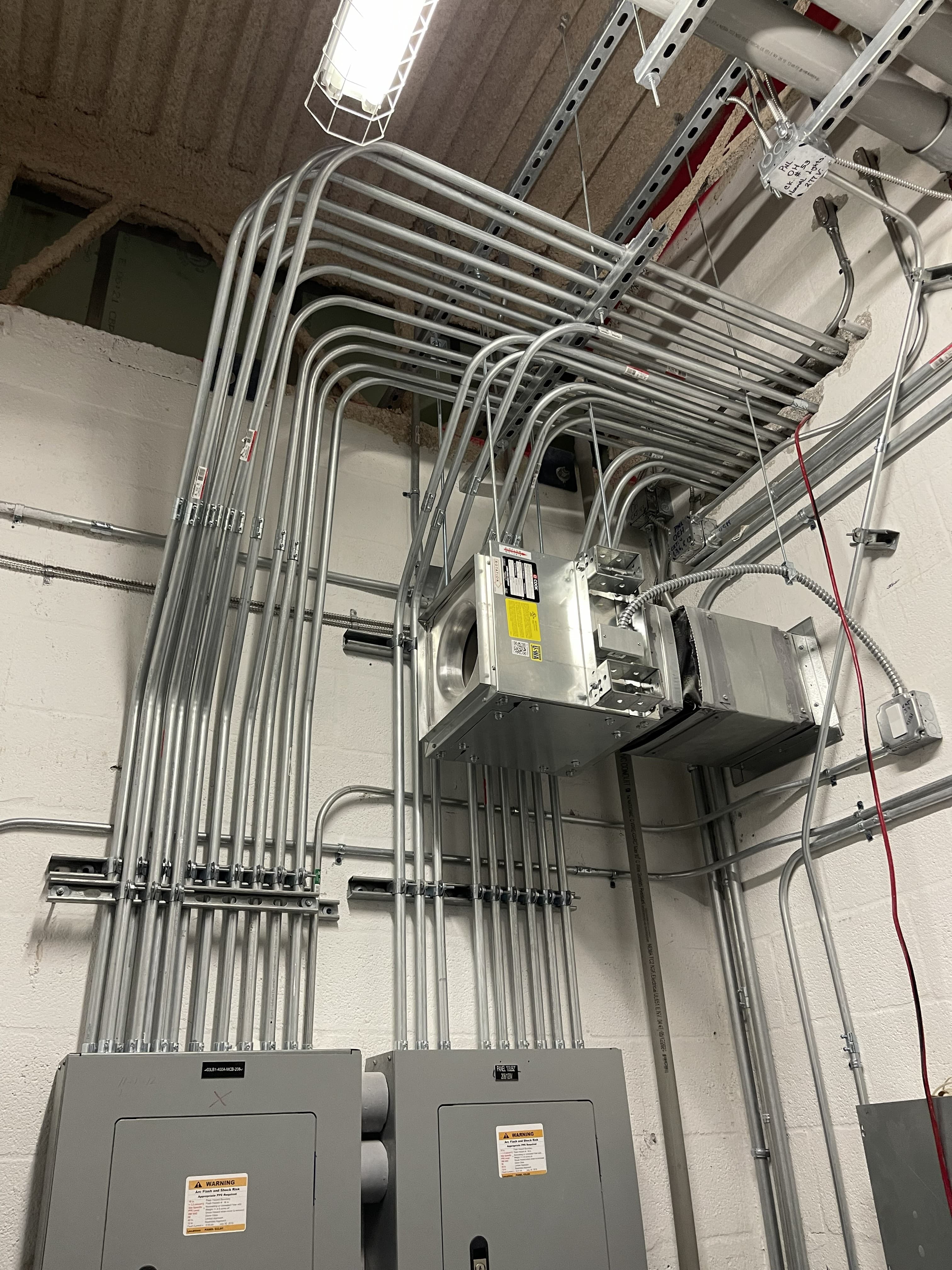 Rigid conduit routed from an overhead junction enclosure down to a pair of panelboards in an electrical room