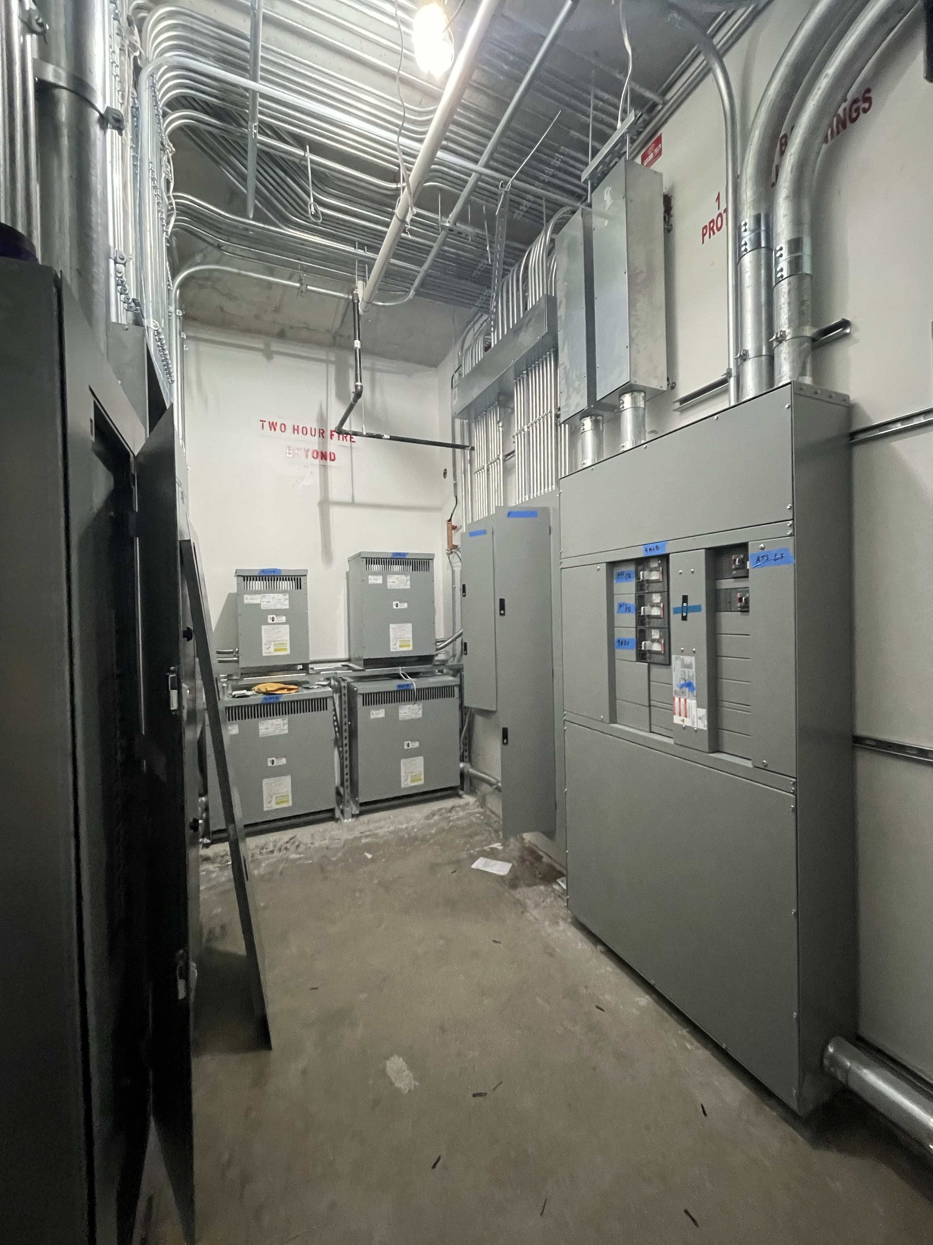 Electrical room with panelboards, transformers, and overhead conduit distribution
