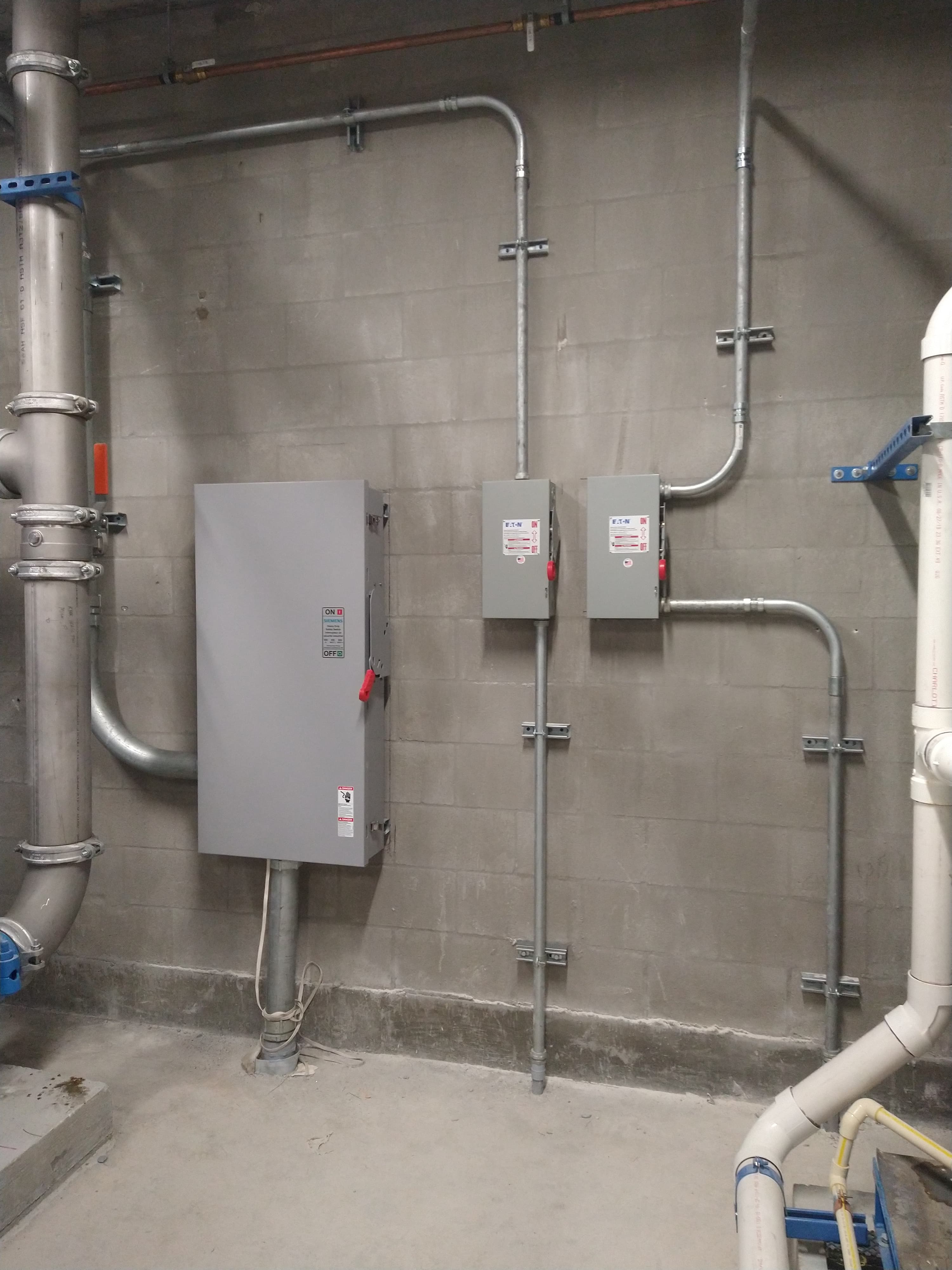 Electrical service disconnect switches mounted on a wall with routed conduit feeding each one