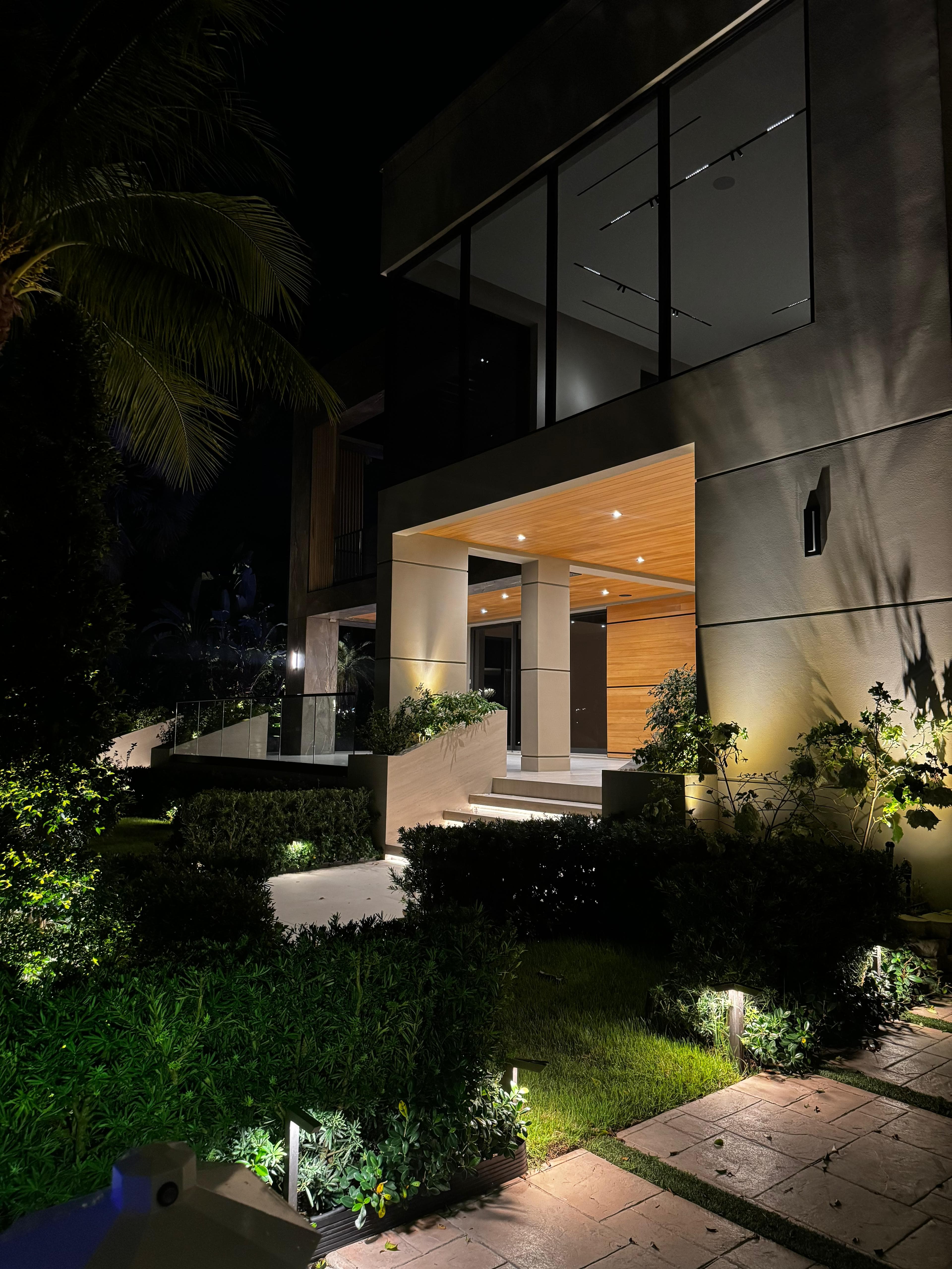 Night exterior of a modern home showing architectural entry lighting and landscape illumination